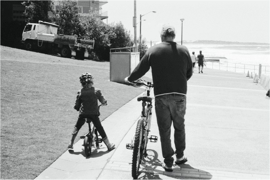 Sydney: a man and a child walking their bicycles down the beach promenade, seen from behind.