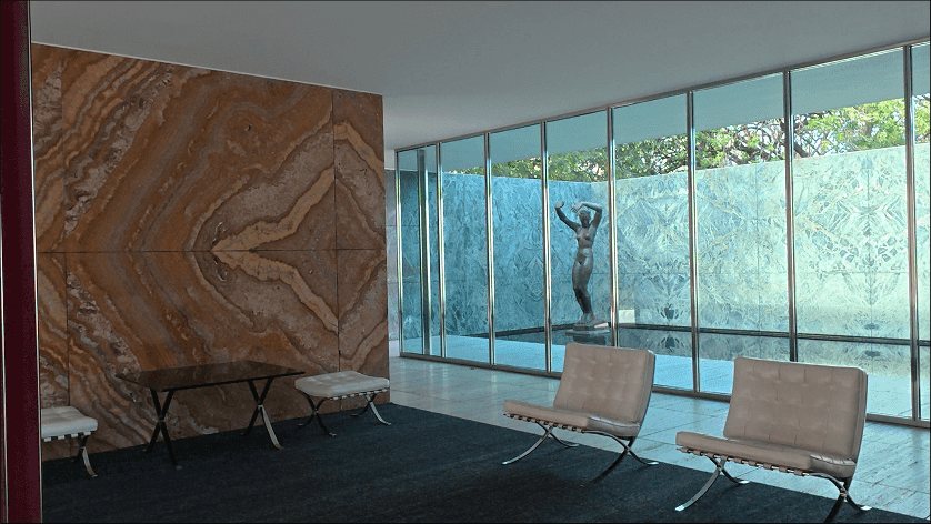 Barcelona Pavilion: the golden onyx wall with two Barcelona chairs, the figure in the water court beyond.