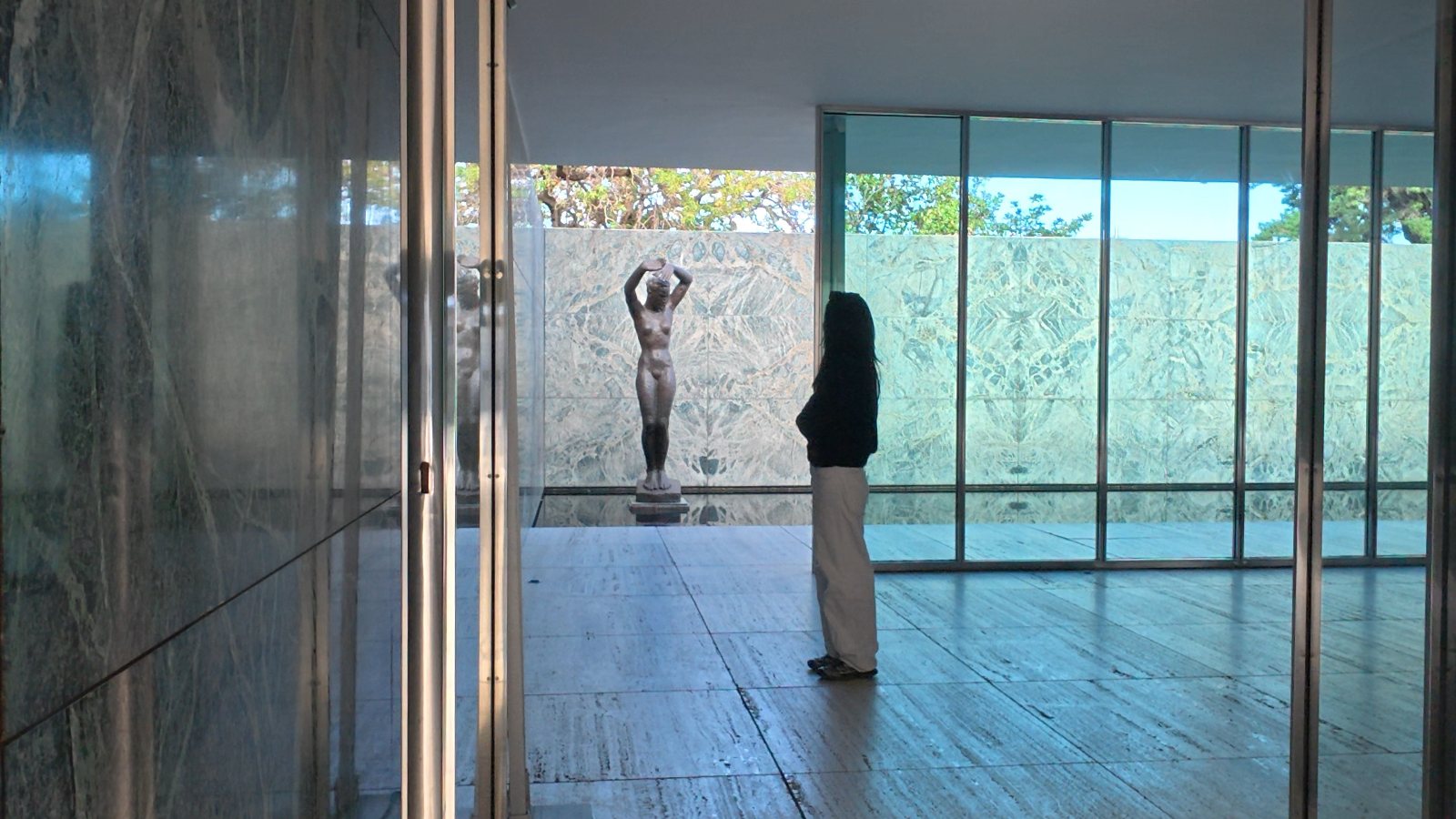 Barcelona Pavilion: a visitor stands before the bronze figure, seen through glass and green marble.